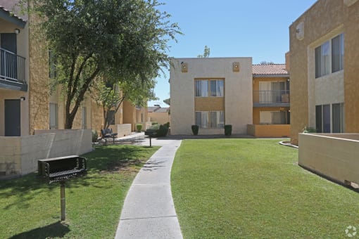 a walkway between two apartment buildings with a lawn and a tree at Melrose Villas, AZ, 85016