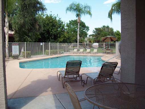 A pool surrounded by a fence with chairs and a table.