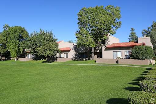 A building with a red roof is surrounded by trees and a green lawn.
