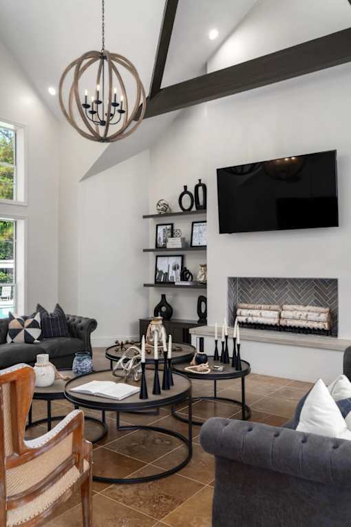 A modern living room with a grey sofa, a wooden chair, a black coffee table, a fireplace, and a TV mounted on the wall.