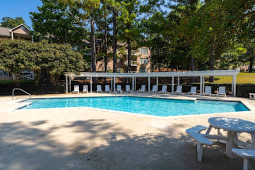 A pool with a white canopy and white chairs.