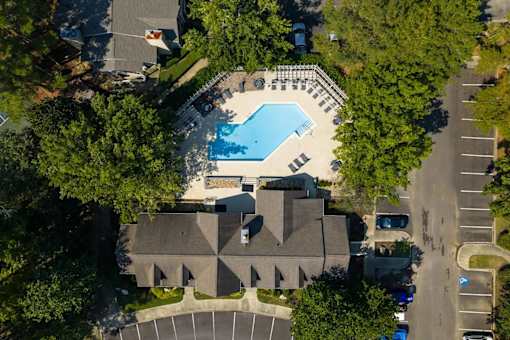 An aerial view of a swimming pool surrounded by trees and a building.