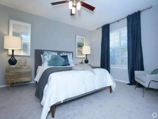 A bedroom with a bed, two lamps, a chair, and a ceiling fan.