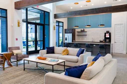 A modern living room with a white sofa set and a kitchen area in the background.