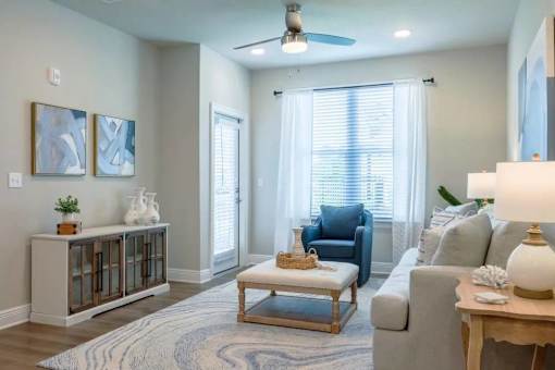 A living room with a grey couch, a glass coffee table, and a ceiling fan.