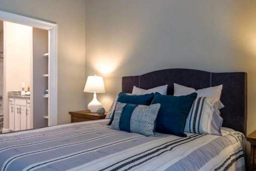 A bed with a white and blue striped comforter and a black headboard with four blue and white pillows.