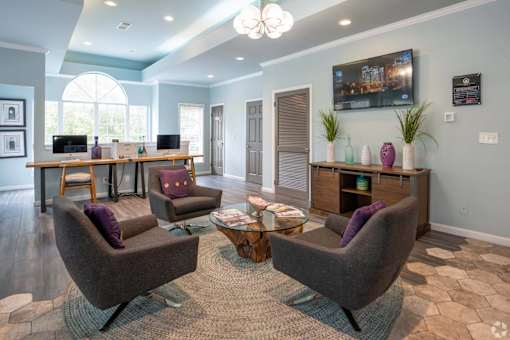 A living room with a large window, a desk, and a TV mounted on the wall.