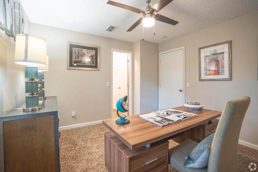 A room with a ceiling fan and a desk with a chair.