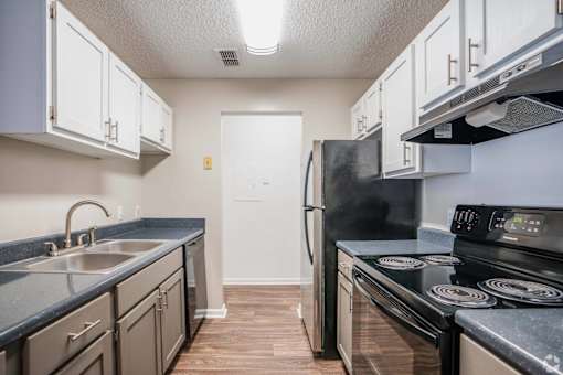 A kitchen with a black refrigerator and stove top oven.