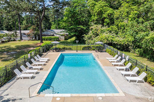 A large swimming pool surrounded by white lounge chairs and green trees.