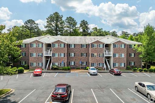 A parking lot in front of a brick building with cars parked.