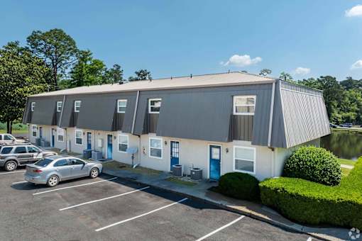 A grey building with a parking lot in front.