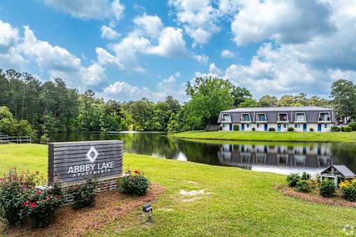 A sign that says Abbey Lake in front of a house and a lake.