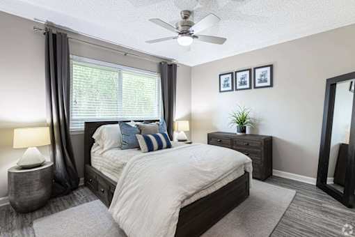 A bedroom with a large bed, a ceiling fan, and a window with curtains.
