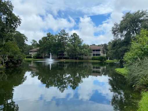 A serene lake surrounded by lush greenery and a building in the distance.