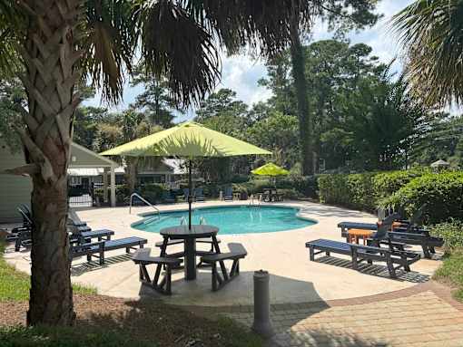 A pool surrounded by trees and a picnic table.