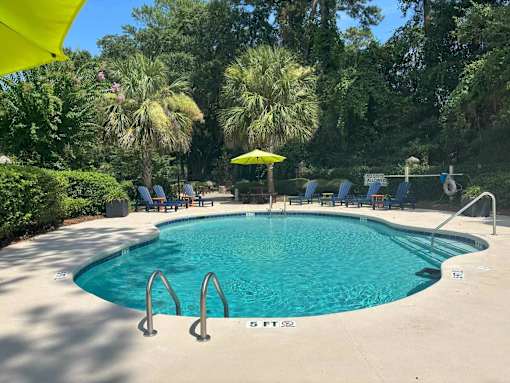 A swimming pool surrounded by trees and chairs.