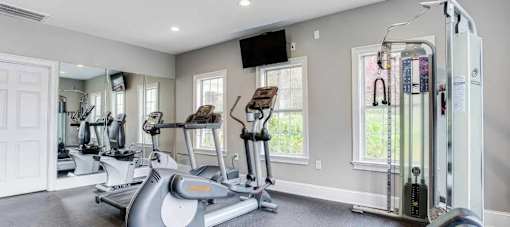 A spacious home gym with a treadmill, elliptical machines, and a television.