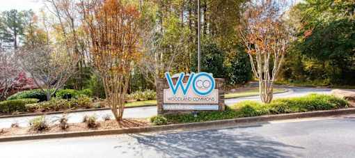 A sign for Woodland Commons is displayed in front of some trees.