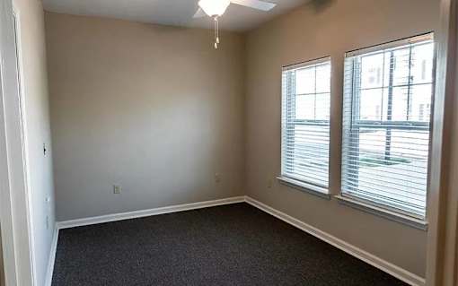 A room with a carpeted floor, a window with blinds, and a ceiling fan.