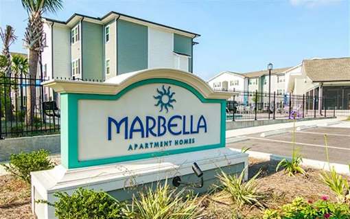 A sign for Marbella Apartment Homes in front of some buildings.