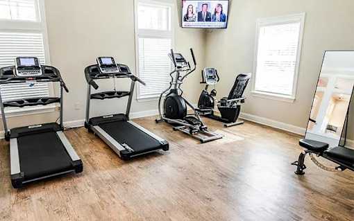 A gym room with treadmills, elliptical machines, and a television screen.
