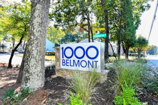 A sign that says 1000 Belmont is in front of a tree.