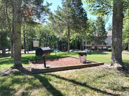 A park with a bench and a trash can.