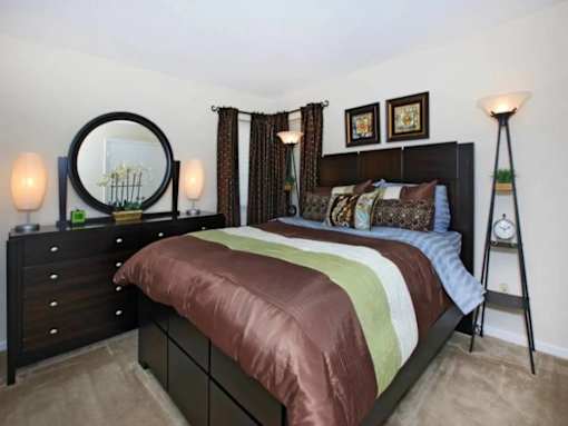 A bedroom with a brown bedspread and a mirror on the dresser.