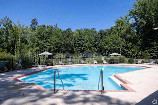 A swimming pool surrounded by trees and chairs.