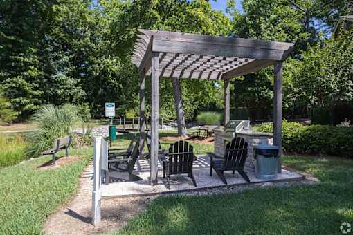 A wooden pergola with a sign and a trash can is in the middle of a grassy area.