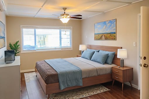 A bedroom with a bed, nightstand, and a painting on the wall.