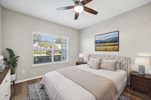 A bedroom with a large bed, a ceiling fan, and a painting on the wall.