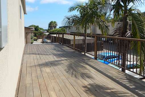 A wooden deck with a pool and palm trees in the background.