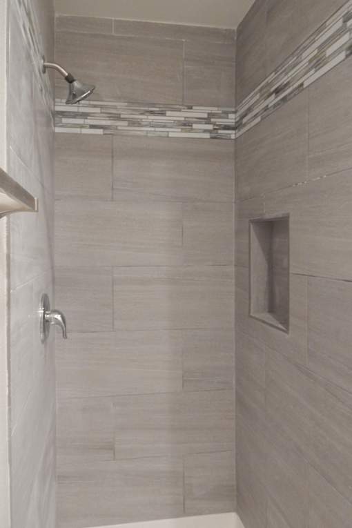 A shower area with a glass door and a wall of tiles.