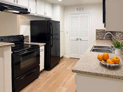 A kitchen with black appliances and a bowl of fruit on the counter.
