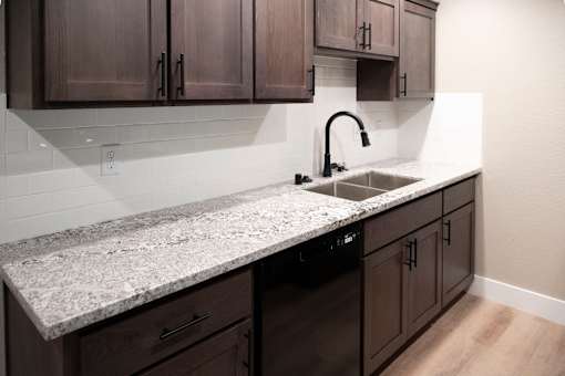 A kitchen with a granite countertop and dark brown cabinets.