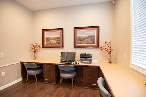 A room with a desk, chairs, and two framed pictures on the wall.