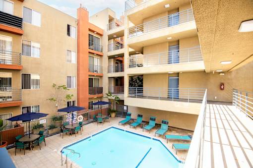 A small pool in a courtyard surrounded by chairs and umbrellas.