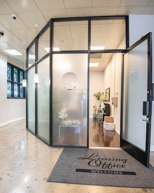 A glass enclosed office with a mat on the floor that says Leasing Office Welcome.