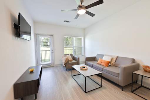 A living room with a grey couch, a coffee table, and a flat screen TV mounted on the wall.