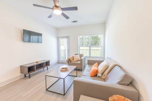 A living room with a grey couch, a coffee table, and a flat screen TV mounted on the wall.