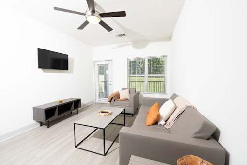 A living room with a grey couch, a black TV, and a ceiling fan.