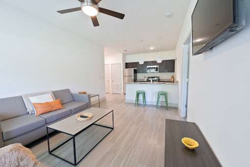 A modern living room with a grey sofa, a glass coffee table, and a flat screen TV mounted on the wall.