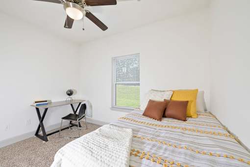 A bedroom with a bed, desk, chair, and window.