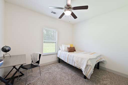 A bedroom with a bed, desk, chair, and window.
