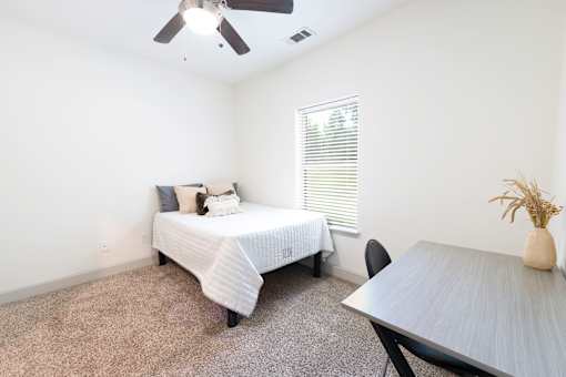 A bedroom with a bed, table, and chair.