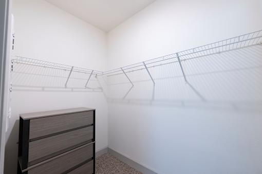 A white closet with a wire shelving unit and a brown dresser.