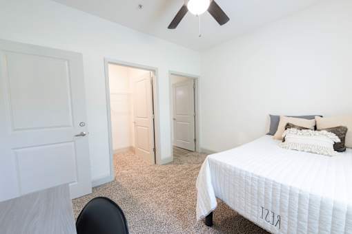 A bedroom with a bed, chair, and a ceiling fan.