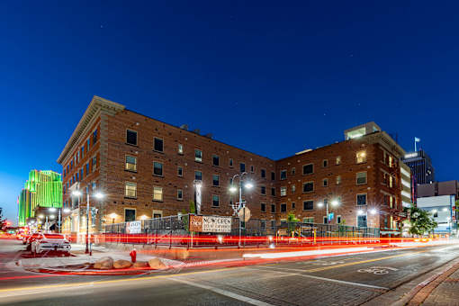 A street view of a city at night with a building in the background and a red fence in the foreground.